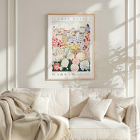 a framed poster of a flower market in Warsaw, Poland, hanging on a white wall above a white couch with a blanket draped over it.