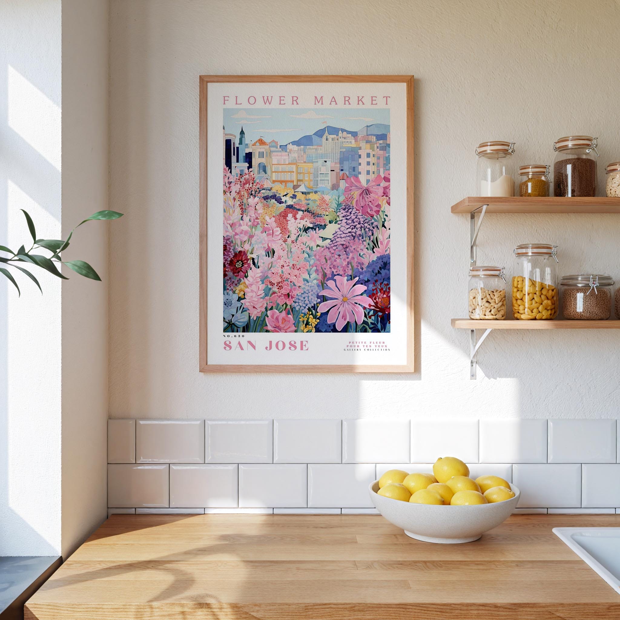 a framed poster of a colorful floral scene hanging on a wall above a kitchen counter with a bowl of lemons and jars of food.