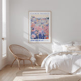 a bedroom with a bed, a woven chair, and a framed poster of a flower market on the wall.