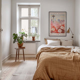 a cozy bedroom with a large bed, a nightstand with a plant, and a framed poster of the Seattle Flower Market on the wall.