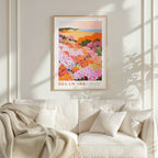 a framed poster of a colorful floral landscape hanging on a wall above a white couch with a blanket draped over it.