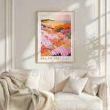 a framed poster of a colorful floral landscape hanging on a wall above a white couch with a blanket draped over it.
