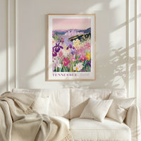 a framed poster of a colorful garden scene with flowers and a cityscape in the background, hanging on a wall above a white couch.