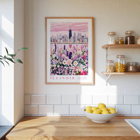 a framed poster of a city skyline with a field of flowers in the foreground, hanging on a wall above a kitchen counter with a bowl of lemons and other kitchen items.