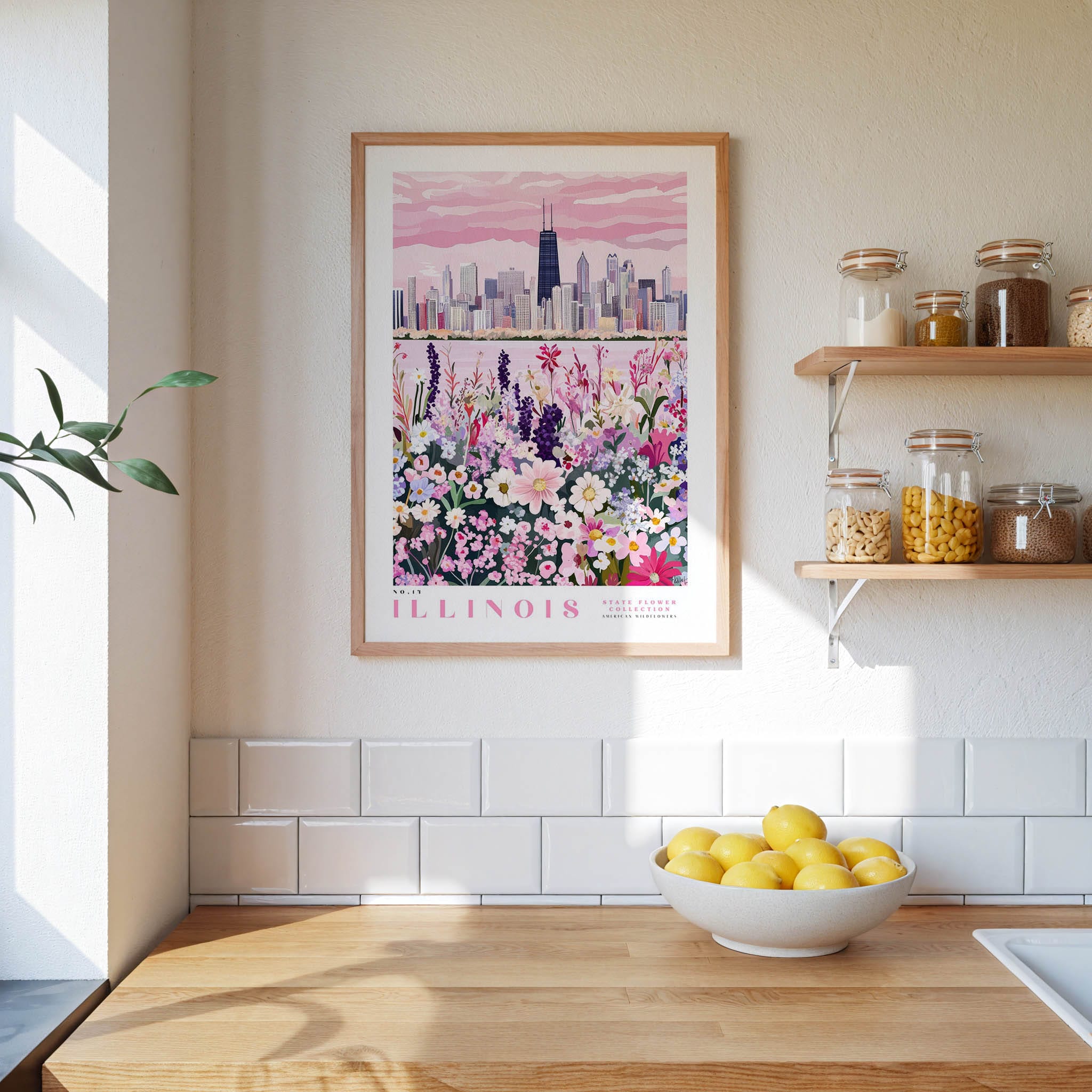 a framed poster of a city skyline with a field of flowers in the foreground, hanging on a wall above a kitchen counter with a bowl of lemons and other kitchen items.