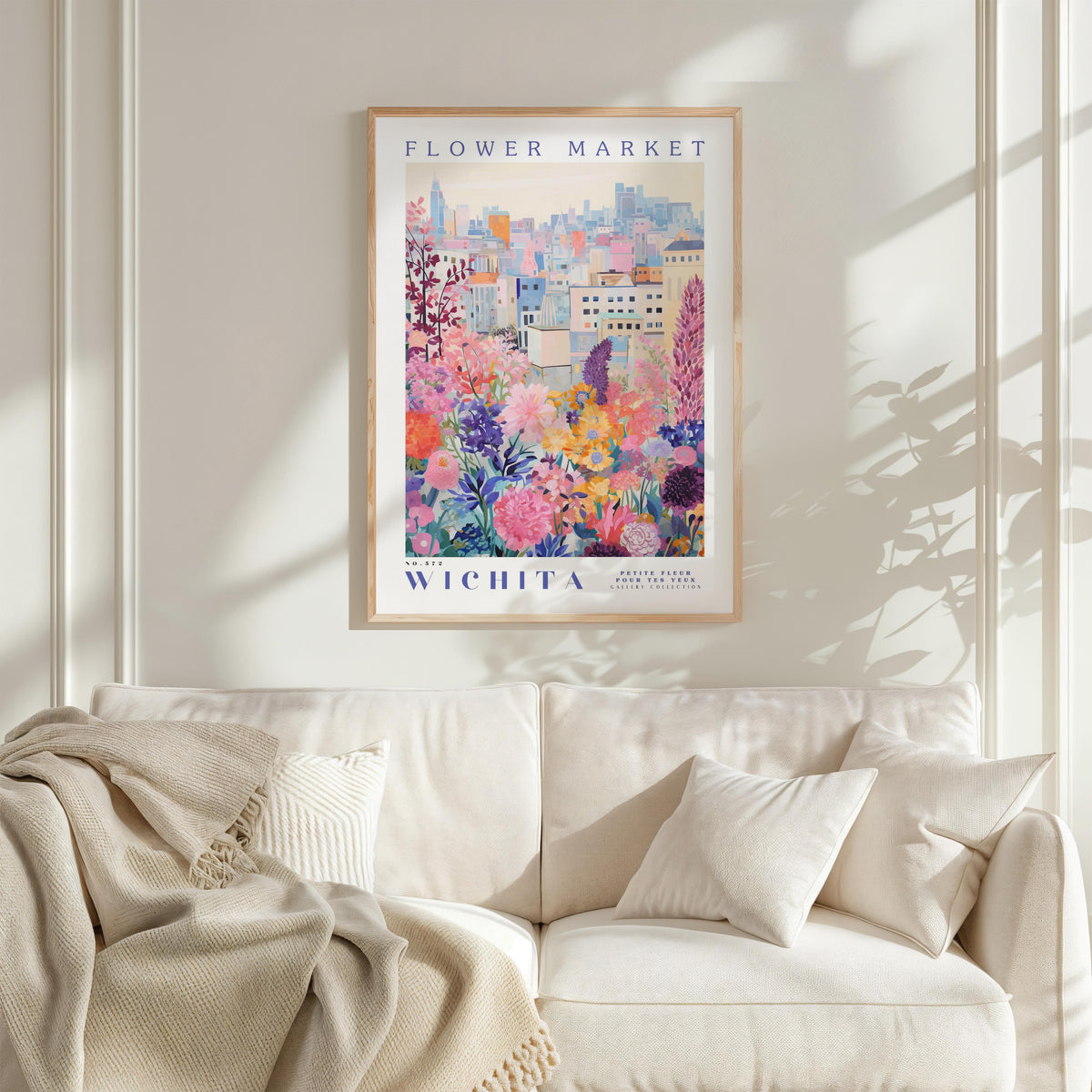 a framed poster of a colorful cityscape with flowers, hanging on a wall above a white couch with pillows.