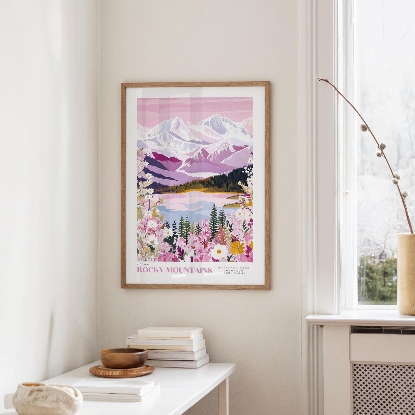 a framed poster of a mountain landscape with a lake and flowers hanging on a wall in a room.