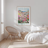 a bedroom with a bed, a wicker chair, and a framed poster of a flower market in Mendocino, Spain.