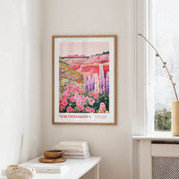 a framed poster of a colorful landscape with flowers hanging on a wall in a room.