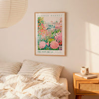 a bedroom with a bed, a nightstand, and a framed poster of a flower market hanging on the wall.