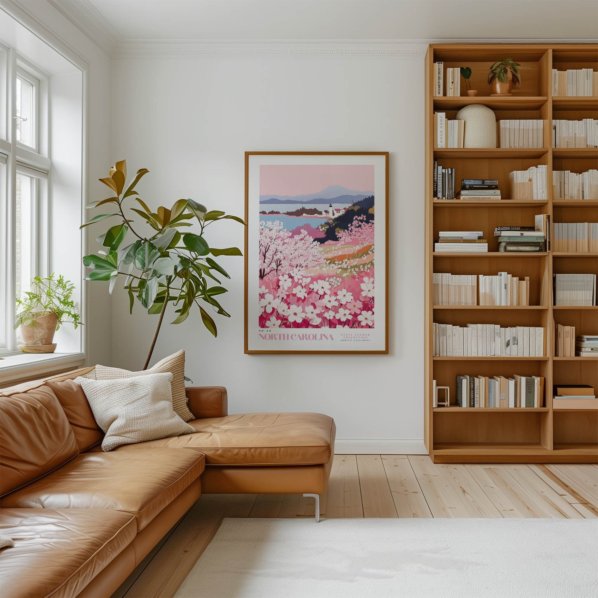 a cozy living room with a large window, a comfortable leather sofa, a wooden bookshelf filled with books, and a framed poster of a floral landscape hanging on the wall.