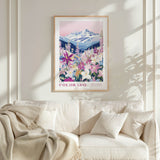 a framed poster of a mountain landscape with a field of colorful flowers, hanging on a wall above a white couch with pillows.