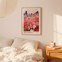 a bedroom setting with a framed poster of a flower market hanging on the wall above a bed with striped pillows.