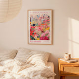 a bedroom setting with a framed poster of a colorful flower market hanging on the wall above a bed with striped pillows.