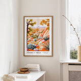 a framed poster of a desert landscape, hanging on a wall in a room with a white table and a window.
