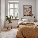 A cozy bedroom with a large bed, a nightstand with a plant, and a framed poster of a flower market on the wall.