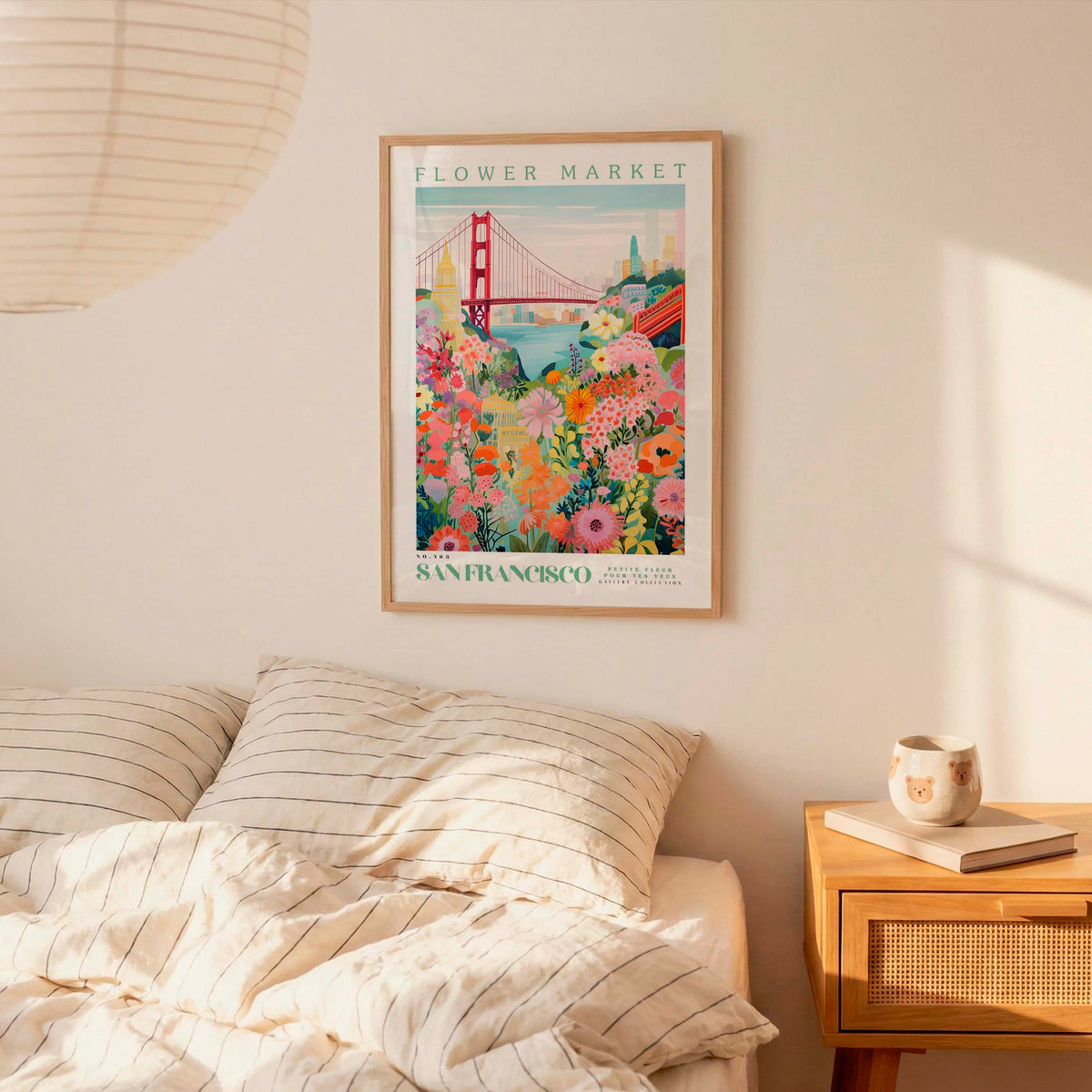 a framed poster of a colorful floral scene hanging on a wall above a bed with striped pillows.