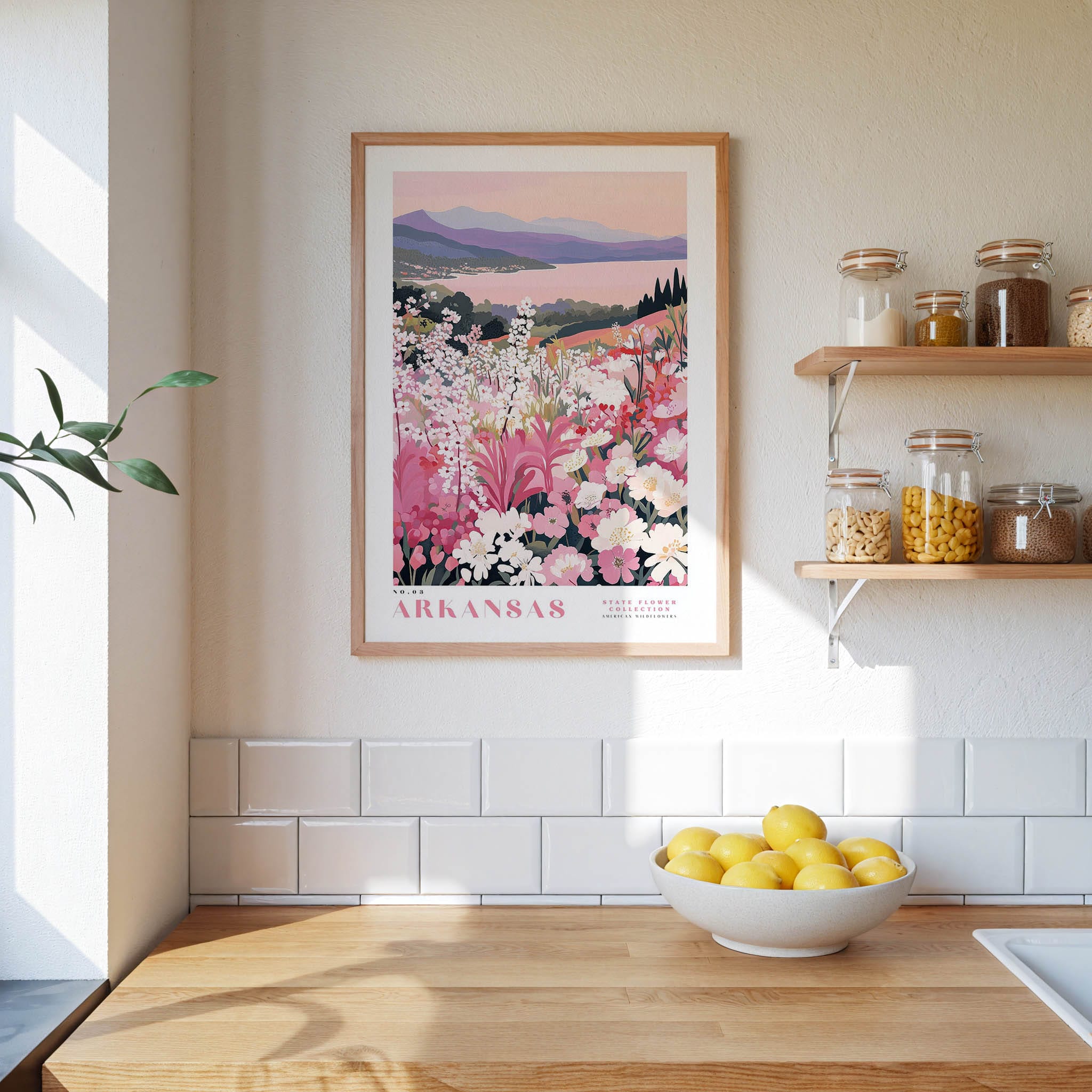 a kitchen scene with a framed poster of a flowery landscape hanging on the wall above a wooden countertop with a bowl of lemons.