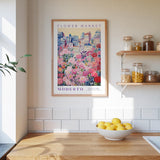 a kitchen counter with a bowl of lemons, a framed poster of a flower market, and shelves with jars and containers.