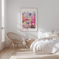 a bedroom with a bed, a wicker chair, and a framed poster of a flower market in Buffalo, New York.