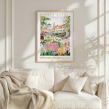 a framed poster of a colorful garden scene hanging on a wall above a white couch with a blanket draped over it.