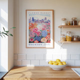 a framed poster of a colorful floral scene hanging on a wall above a kitchen counter with a bowl of lemons on it.