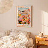 a bedroom setting with a framed poster of a colorful floral scene hanging on the wall above a bed with striped pillows.