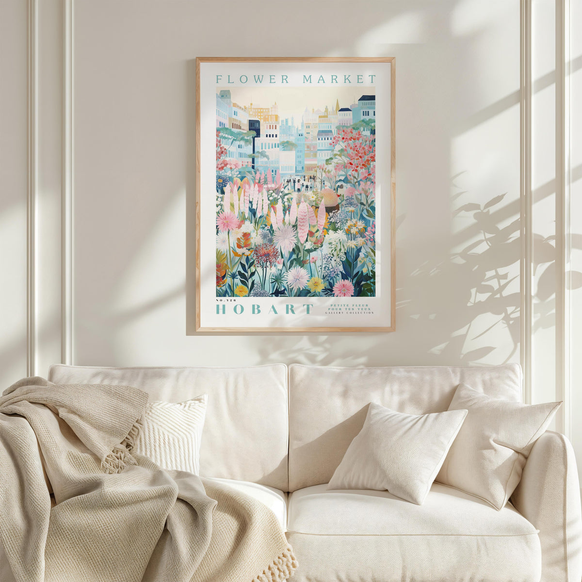 a framed poster of a colorful floral scene hanging on a wall above a white couch with a blanket draped over it.