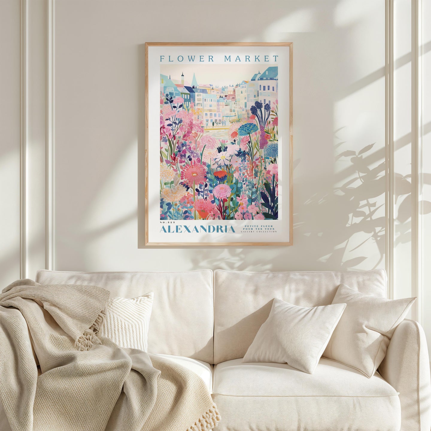 a framed poster of a colorful floral scene hanging on a wall above a white couch with a blanket draped over it.