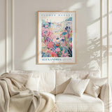 a framed poster of a colorful floral scene hanging on a wall above a white couch with a blanket draped over it.