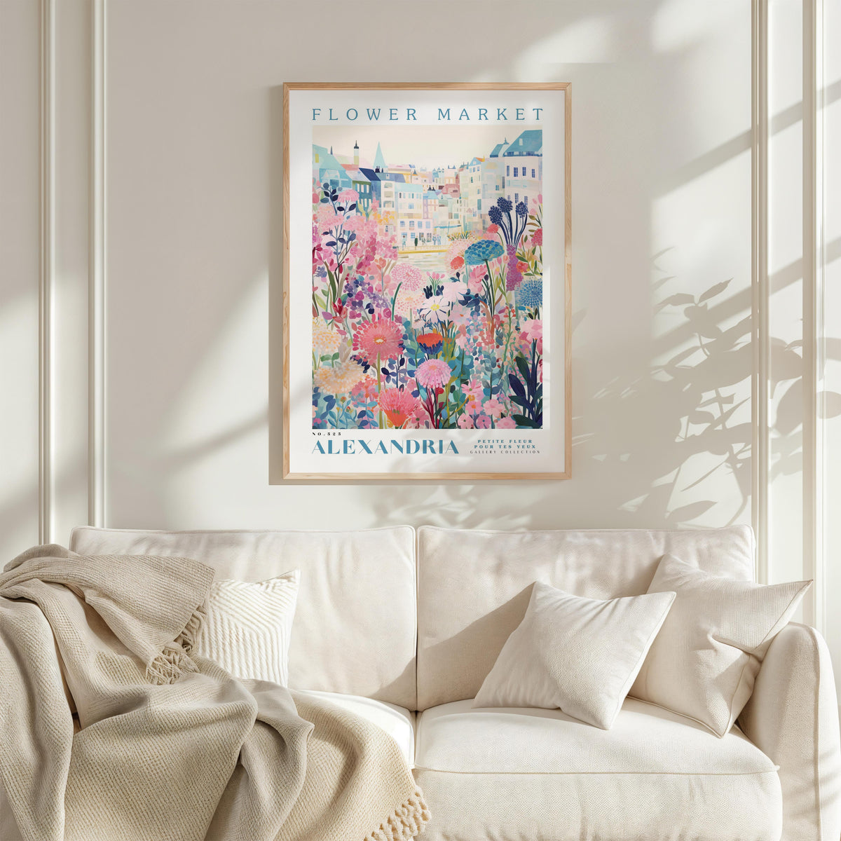 a framed poster of a colorful floral scene hanging on a wall above a white couch with a blanket draped over it.