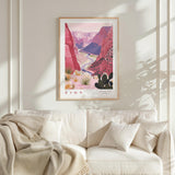 a framed poster of a desert landscape with mountains and cacti, hanging on a white wall above a white couch with a blanket draped over it.