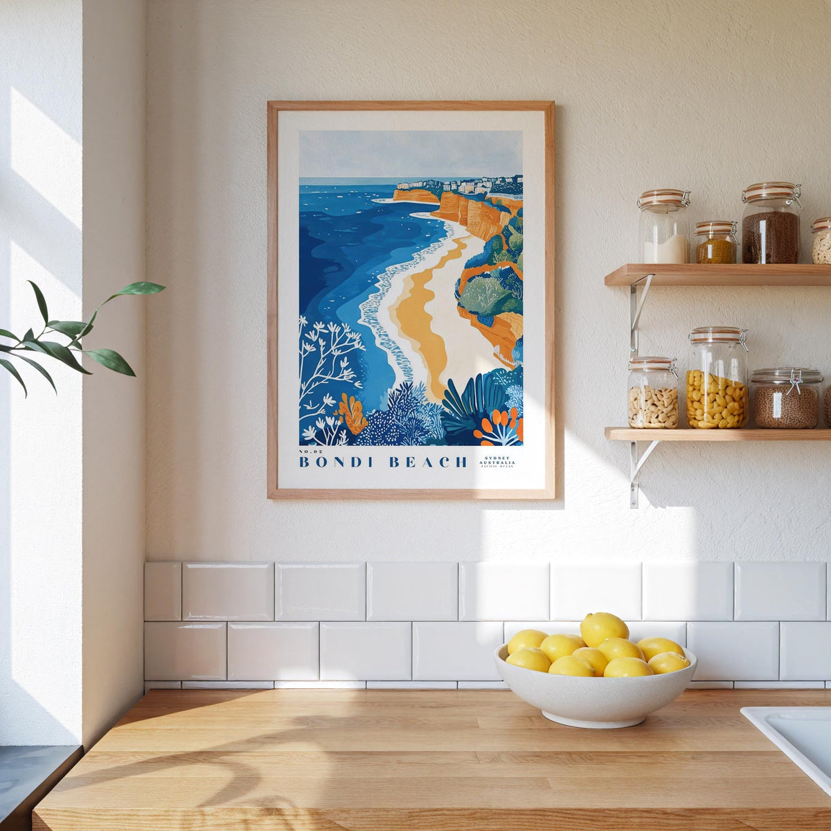 a kitchen counter with a bowl of lemons, a framed poster of Bondi Beach, and shelves with jars and bottles.