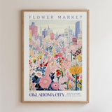 The image is a framed poster depicting a vibrant and colorful cityscape with a variety of flowers and plants in the foreground.