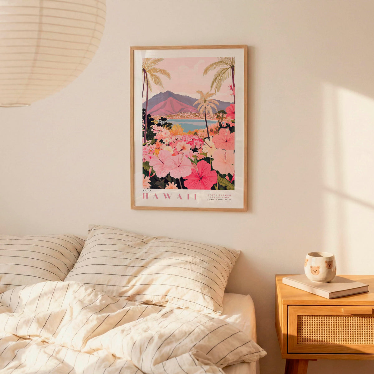a framed poster of a tropical landscape with palm trees, flowers, and mountains, hanging on a wall above a bed with striped pillows.