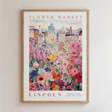 A framed poster depicting a vibrant and colorful flower market in Lincoln, with a cityscape in the background.