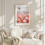 a framed poster of a cityscape with a flower market in the background, hanging on a wall above a white couch with a blanket draped over it.