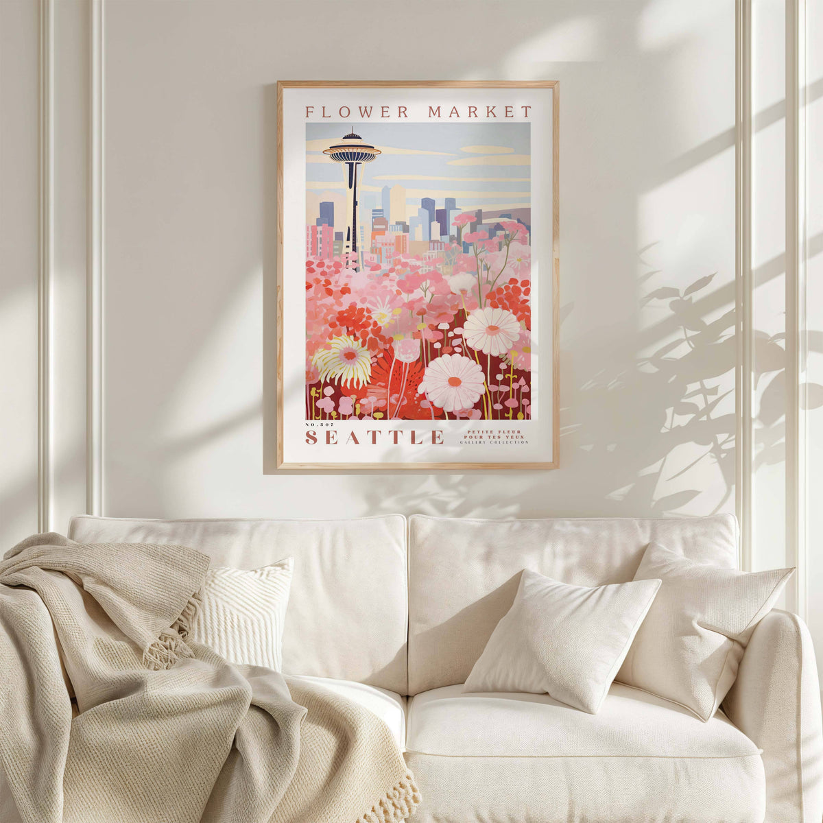 a framed poster of a cityscape with a flower market in the background, hanging on a wall above a white couch with a blanket draped over it.