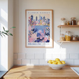 a framed poster of the Brisbane Flower Market, a city in Australia, hanging on a wall above a kitchen counter with a bowl of lemons and other kitchen items.