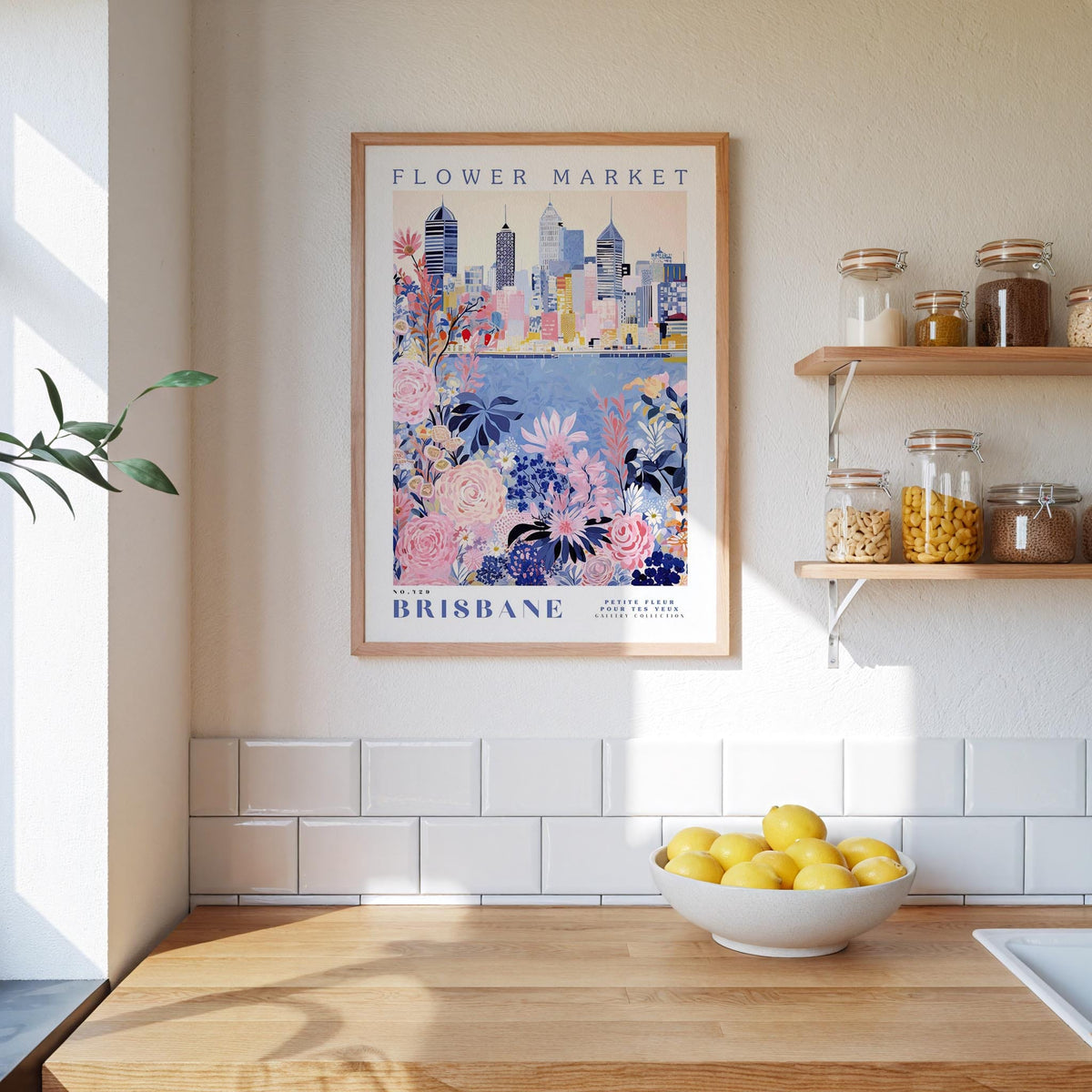 a framed poster of the Brisbane Flower Market, a city in Australia, hanging on a wall above a kitchen counter with a bowl of lemons and other kitchen items.