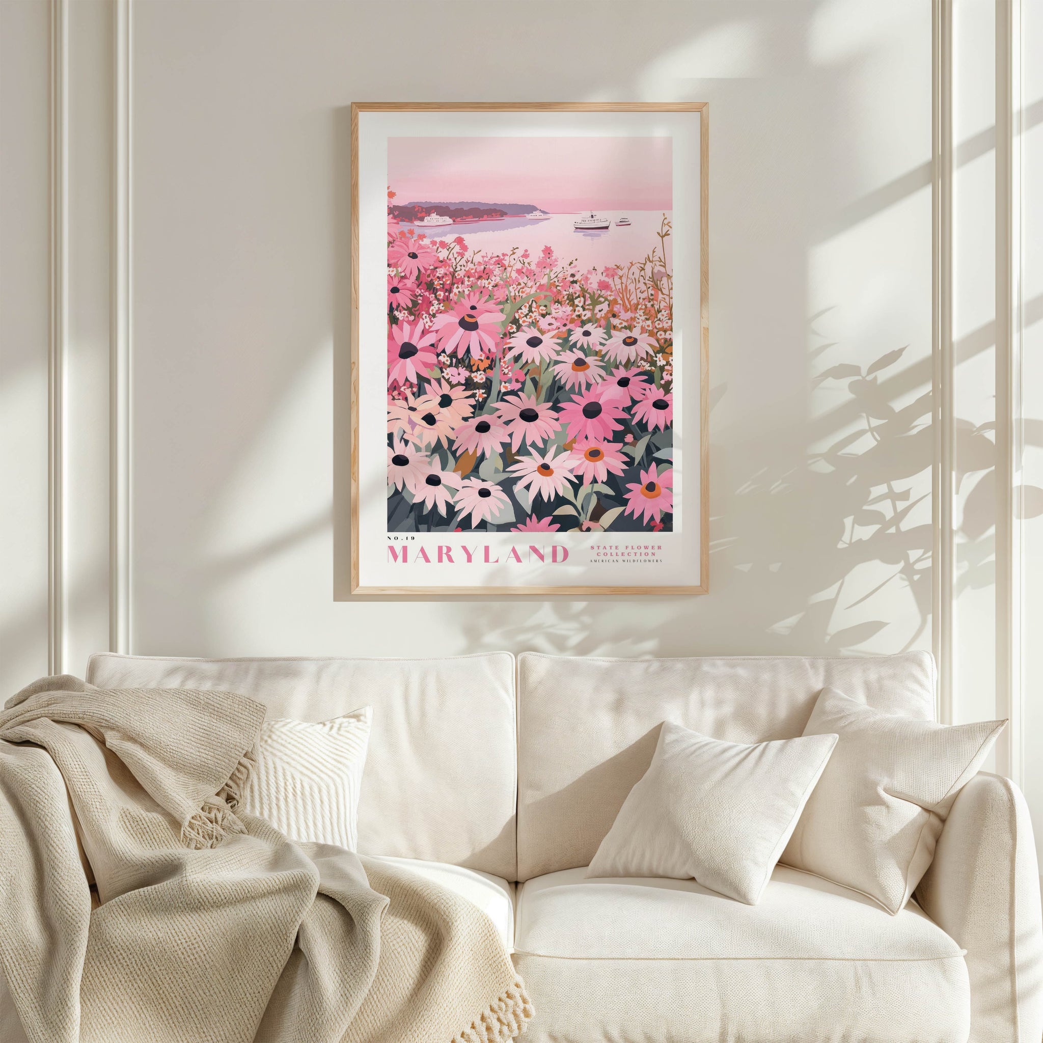 a framed poster of a field of flowers, specifically a field of daisies, hanging on a wall above a white couch.