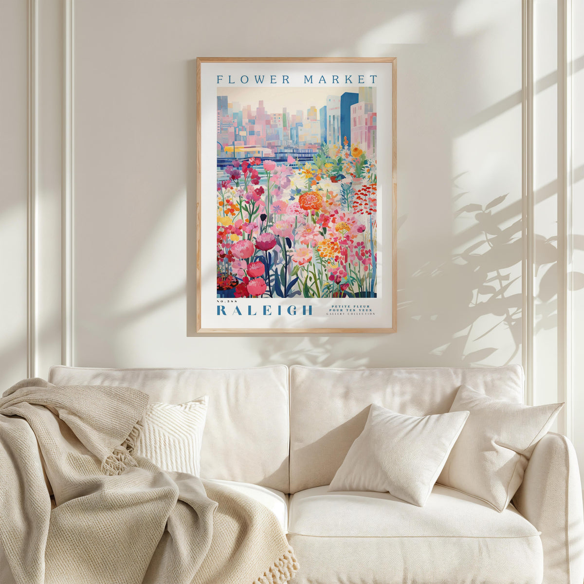 a framed poster of a colorful floral scene hanging on a wall above a white couch with a blanket draped over it.