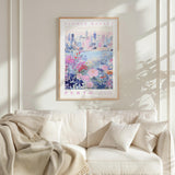 a framed poster of a cityscape with a floral design, hanging on a wall above a white couch with a blanket draped over it.