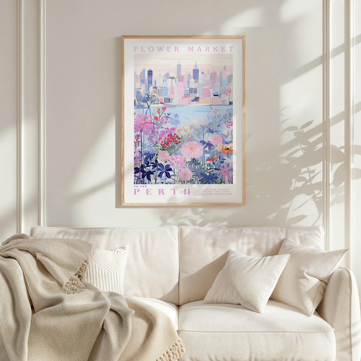 a framed poster of a cityscape with a floral design, hanging on a wall above a white couch with a blanket draped over it.