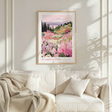 a framed poster of a mountain landscape with pink flowers hanging on a wall above a white couch with a blanket draped over it.