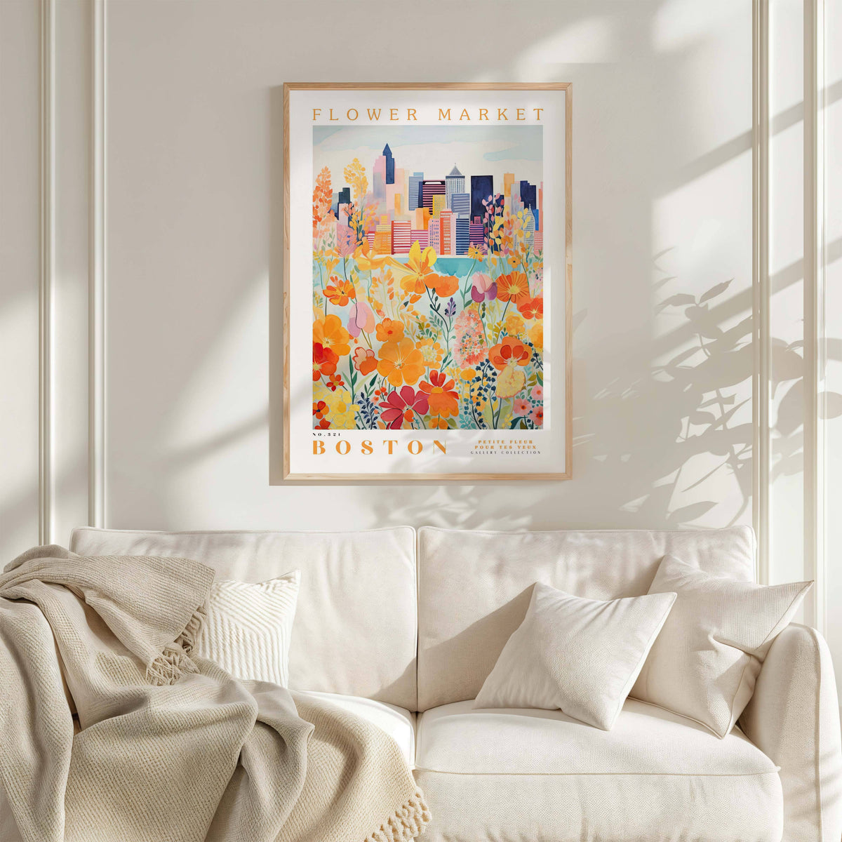 a framed poster of a cityscape with a flower market in the background, hanging on a wall above a white couch with a blanket draped over it.