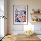 a framed poster of a colorful floral scene hanging on a wall above a wooden countertop with a bowl of lemons.