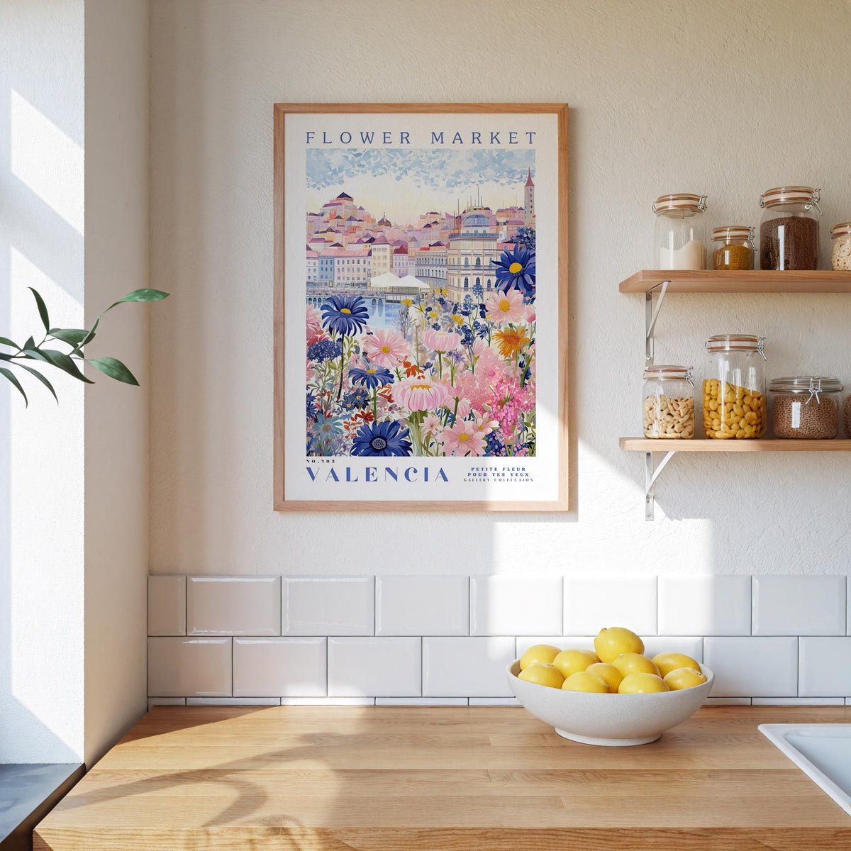 a framed poster of a colorful floral scene hanging on a wall above a wooden countertop with a bowl of lemons.