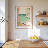 a kitchen scene with a framed poster of a beach, a bowl of lemons, and shelves with jars and bottles.