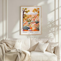 a framed poster of a desert landscape with a tree, hanging on a wall above a white couch with a blanket draped over it.